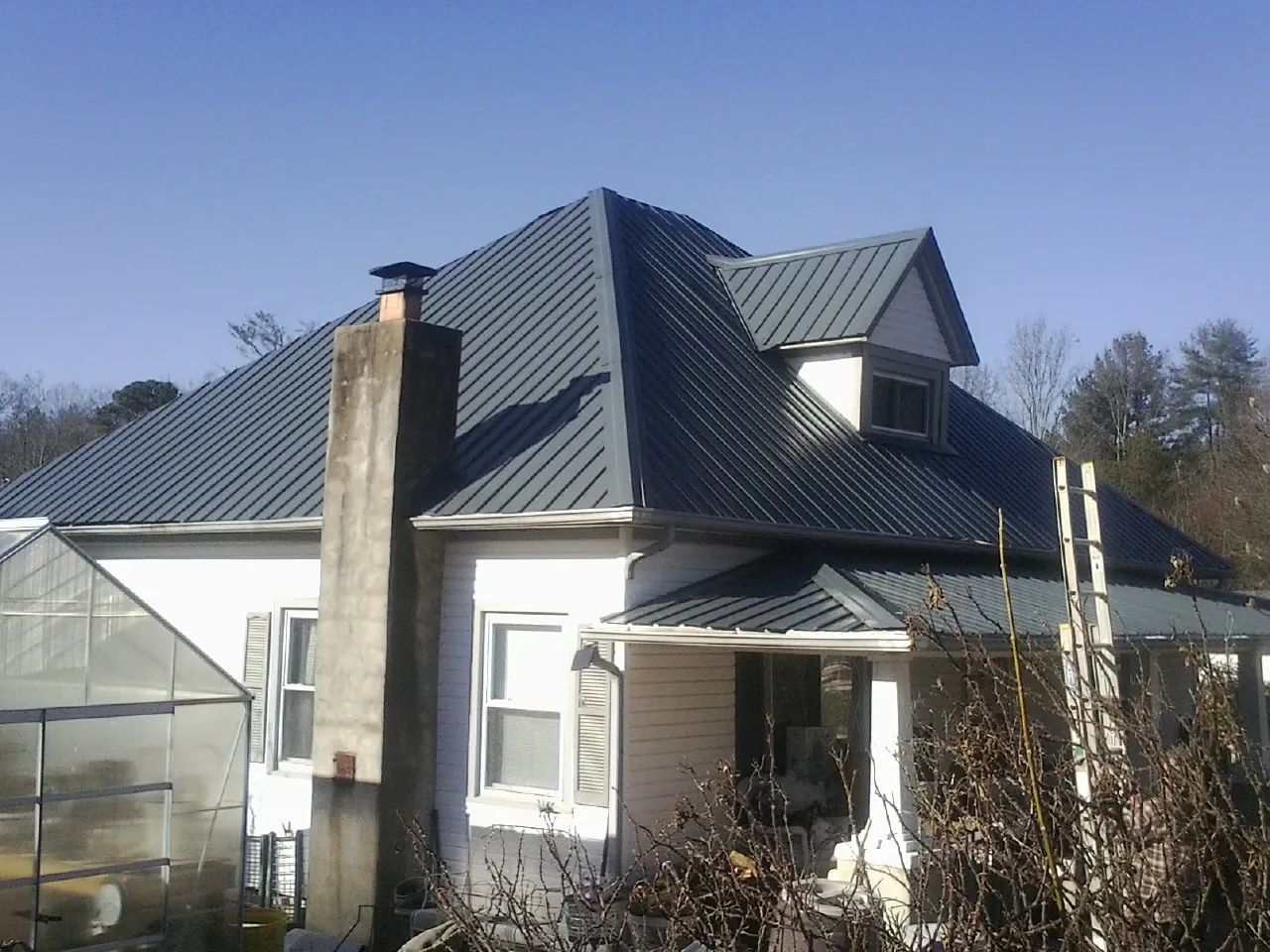 Dark blue standing seam metal roof on a white farmhouse with dormer — Slate & Tile Roof Repair by Roofing Brothers in Lewis