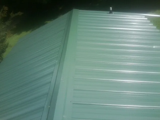 New green metal panels meeting at the ridge of a roof — Flat Roof Repair work by our crew in Lewis
