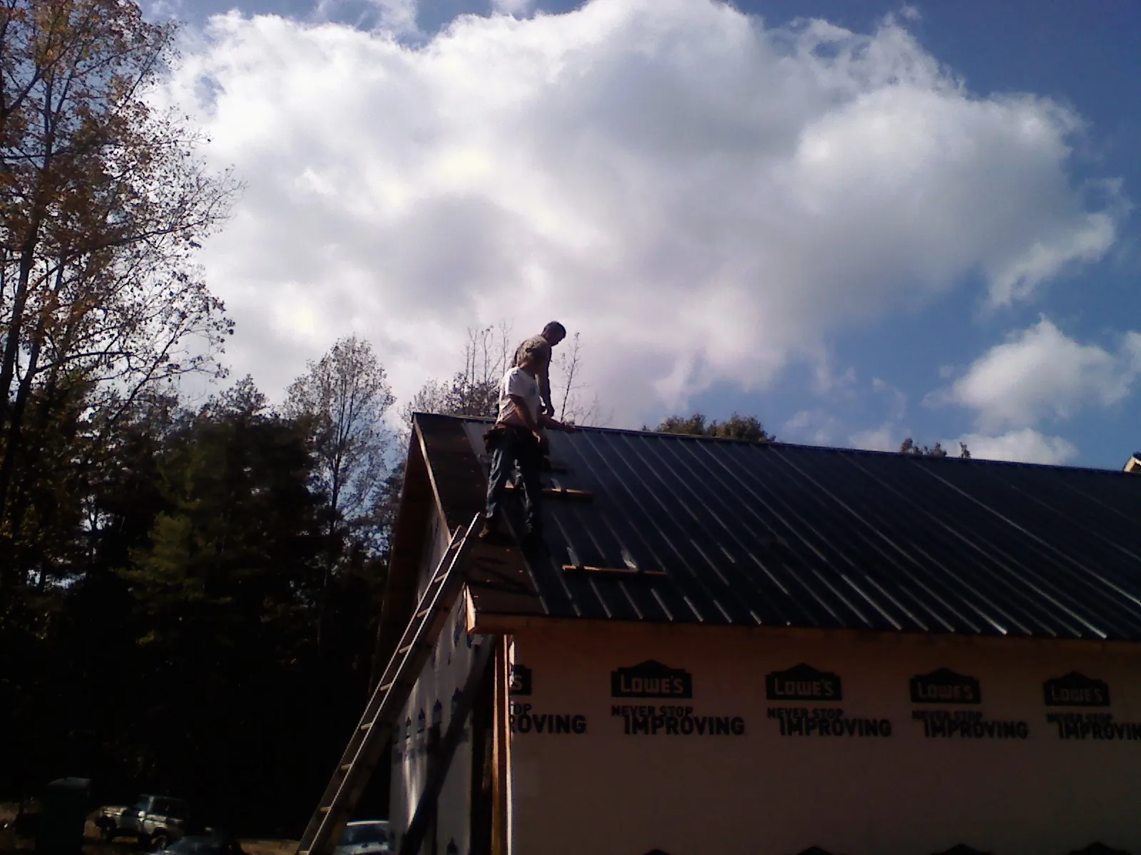 Roofer fastening dark metal panels high against a cloudy sky, from a Roof Inspection job in Lewis