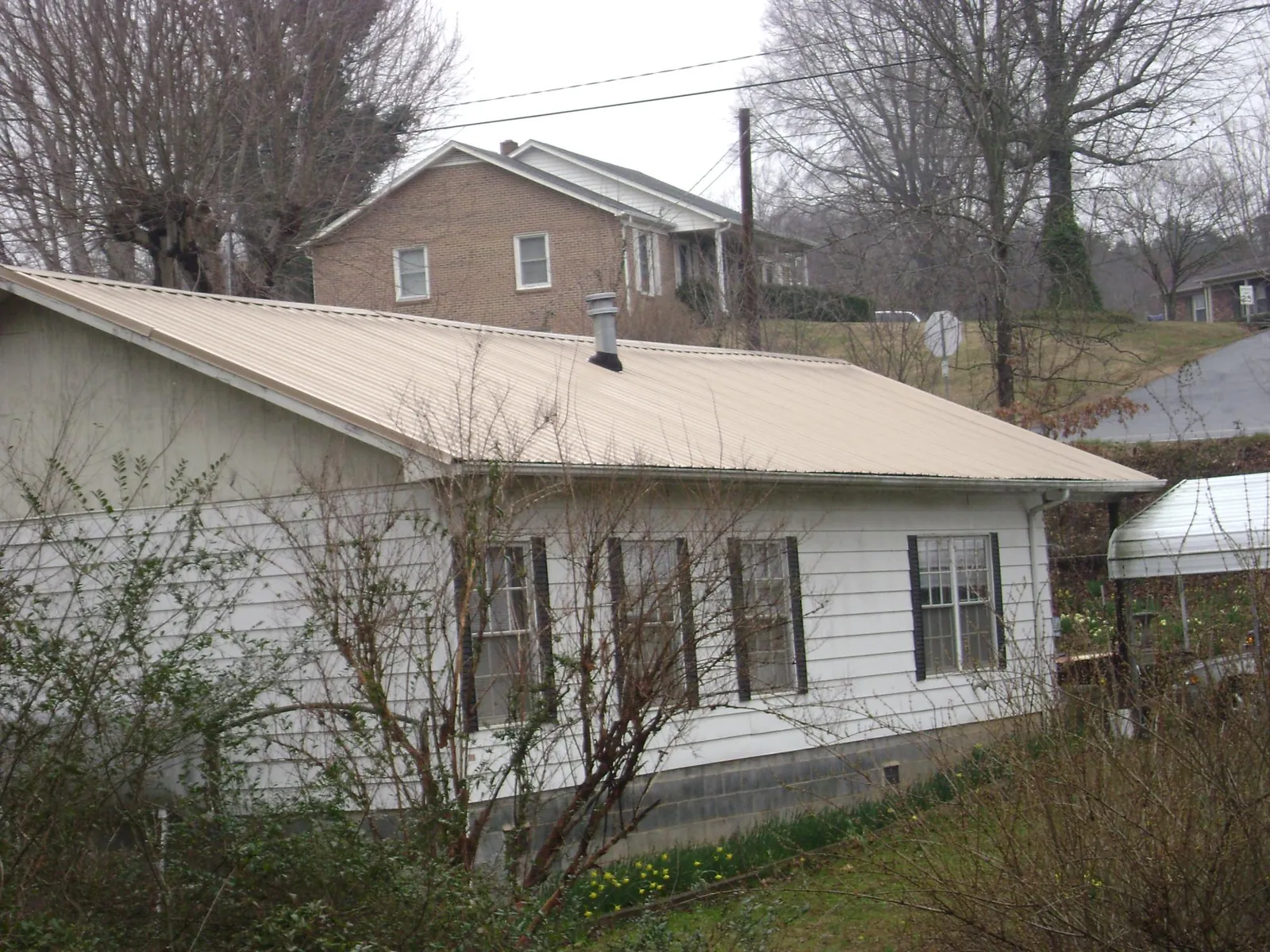 Tan metal roof on a white sided house set into a hillside — Commercial Roofing by Roofing Brothers in Lewis