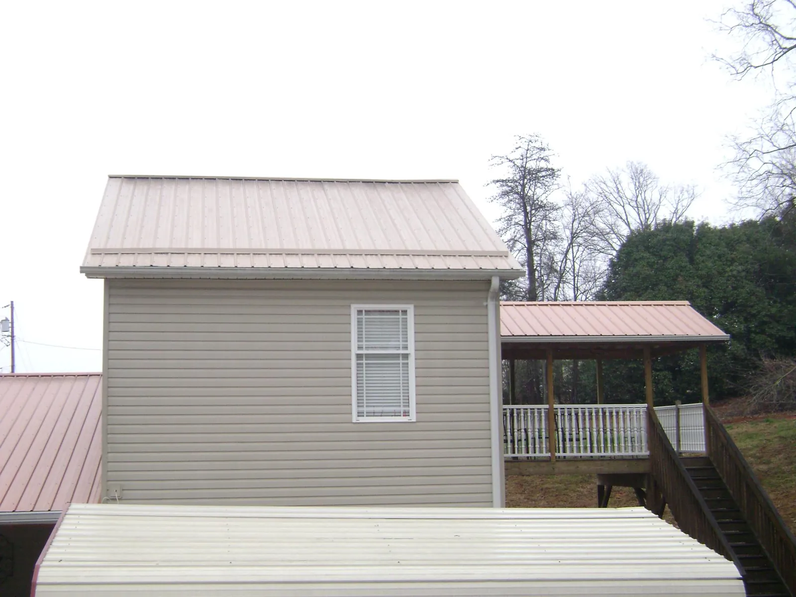 Tan metal roofs on a two story addition and attached porch, from a Roof Replacement job in Lewis